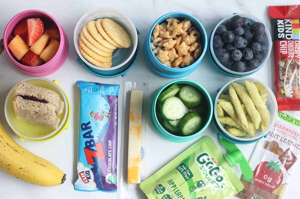 Various fruits, vegetables, and pre-packaged snacks laying on a white table.